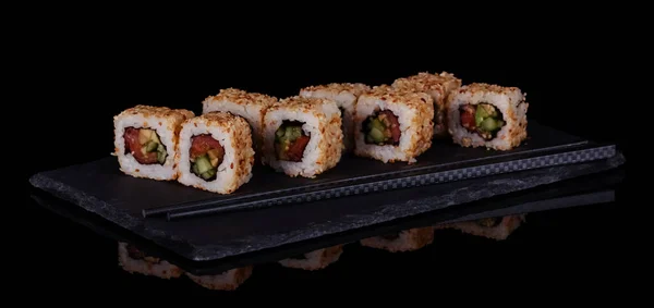 黒を基調とした皿の上にゴマの中に魚介類を盛った寿司巻き — ストック写真
