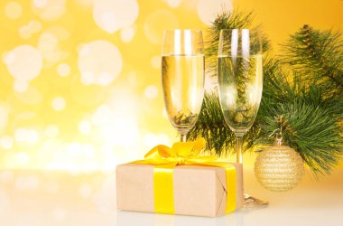 Şampanya kadehleri, Noel hediyesi ve sarı arka planda Noel ağacı.