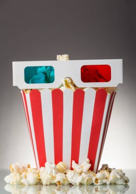 Çizgili bir kutuda patlamış mısır ve gri arka planda 3 boyutlu gözlük.