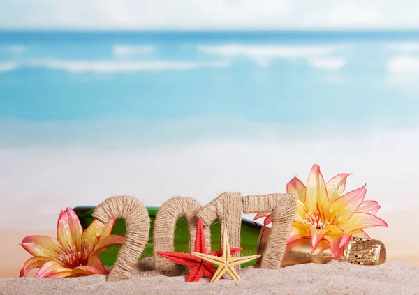 シャンパンのボトルと砂の碑文2017は 海の背景に熱帯の花で飾られています — ストック写真