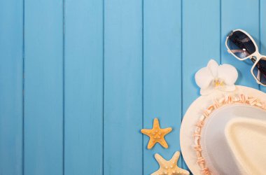 Beach accessories: hat, sunglasses, starfish and orchid flower on wood background painted in blue.