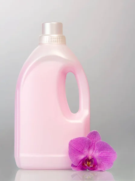 灰色の背景に液体洗剤と蘭の花とピンクのプラスチックボトル — ストック写真
