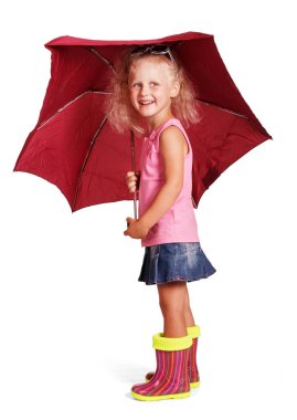 Beyaz arka planda şemsiyesi olan, bluz, etek ve lastik çizme giyen sevimli, neşeli küçük bir kız..
