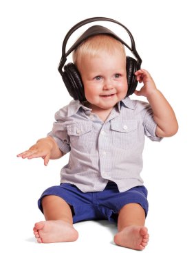 Parlak çizgili tişörtlü, mavi şortlu, kulaklıklı, beyaz arka planda izole edilmiş müzik dinleyen neşeli küçük bir çocuk..