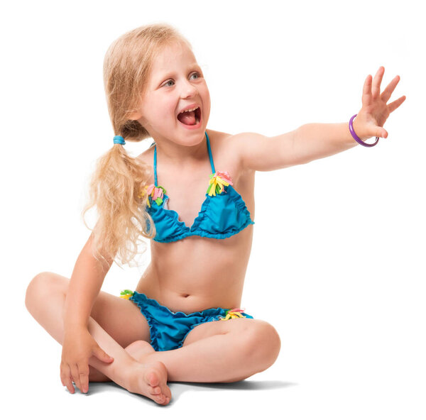 Seated petite blond girl in a swimsuit, her arm stretched forward isolated on white background.