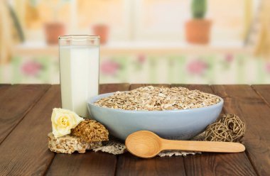 Bir kase yulaf ezmesi, bir bardak süt, bir kaşık ve arka planda bir gül..