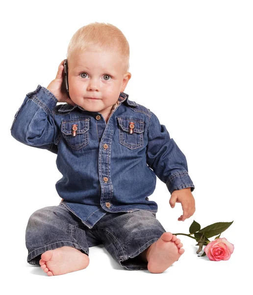 穿着蓝色衬衫和牛仔裤的可爱的小男孩坐在那里拿着一部手机 一束玫瑰花被白色的背景隔开了 — 图库照片