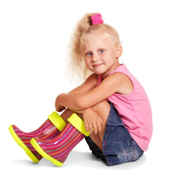 Mała Blondynka Siedzi Różowej Bluzce Niebieskiej Spódnicy Kolorowe Gumowe Buty — Zdjęcie stockowe