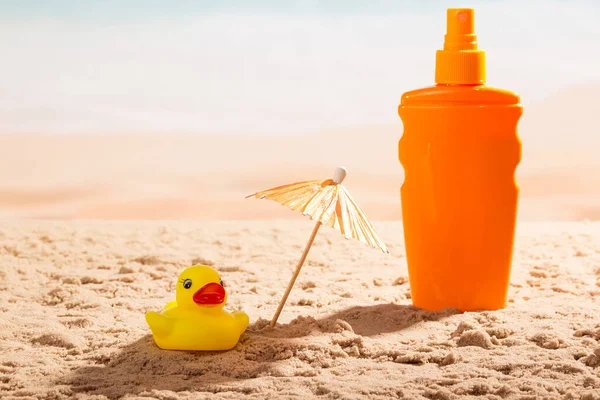 Sunscreen, umbrella and a rubber duck on the seashore.