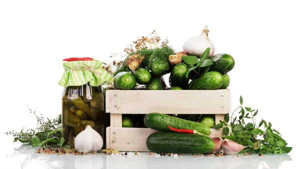 Fresh cucumbers in a wooden box and a jar of pickled spices isolated on a white background.