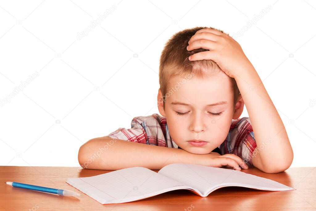 Tired boy sitting at the table fell asleep on exercise book isolated on white background.