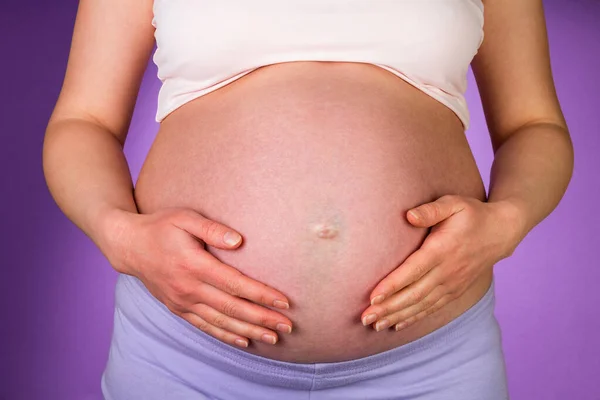 Zwangere Vrouw Omarmen Een Buik Haar Handen Paarse Achtergrond — Stockfoto