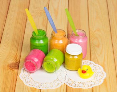 Farklı plastik kaşıklarla cam kavanozlar ve hafif ahşap arka planda plastik ördek..