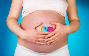 Ivf 'te el ele tutuşan hamile bir kadın mavi arka planda yazı yazıyor..