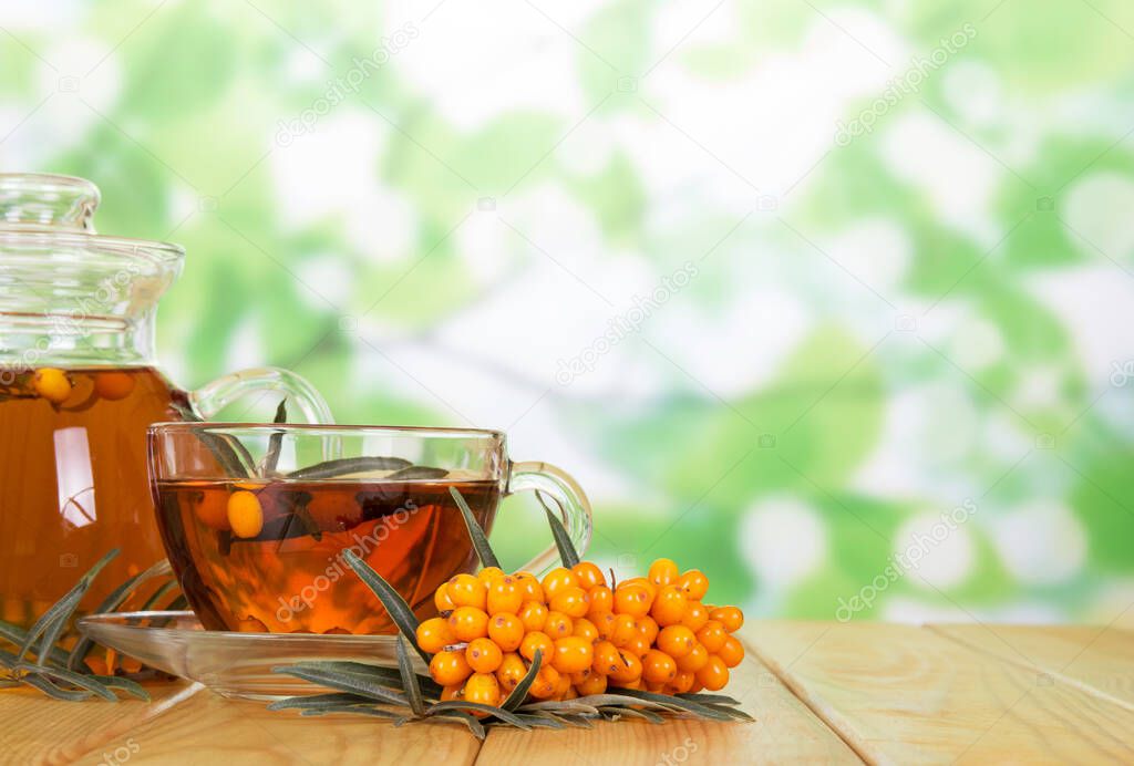 Pitcher and a glass of beverage, bunch of sea buckthorn on abstract green background.