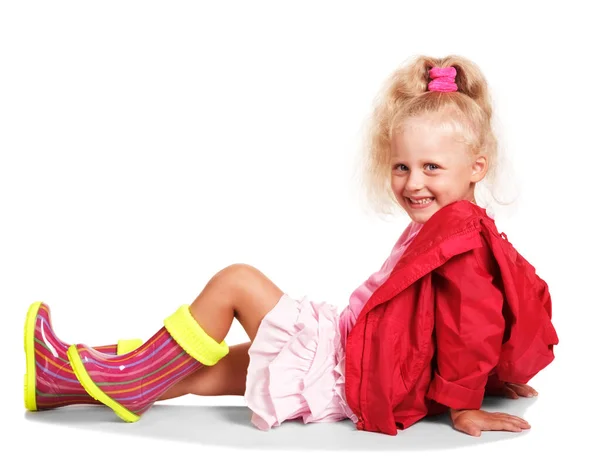 幸せな小さなブロンド女の子で赤ジャケットとカラフルなゴムブーツ ピンクスカート座って隔離された上に白の背景 — ストック写真