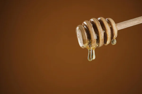 Honey dripping from honey dipper. Thick honey dipping from the wooden honey spoon. yellow background. closeup
