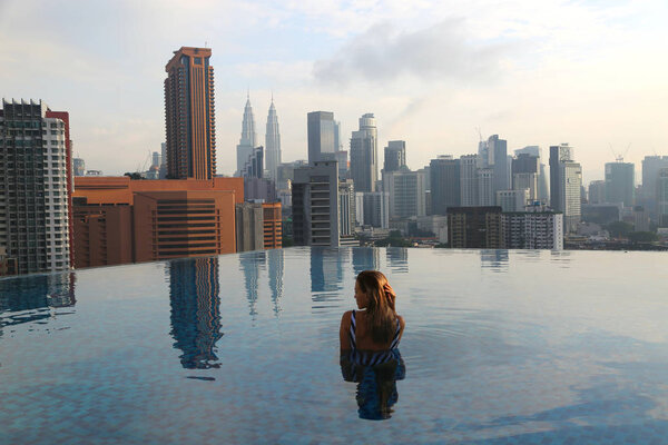 Young happy girl swimming alone in the infinity pool on rooftop early in the morning in Kuala Lumpur in Malaysia.