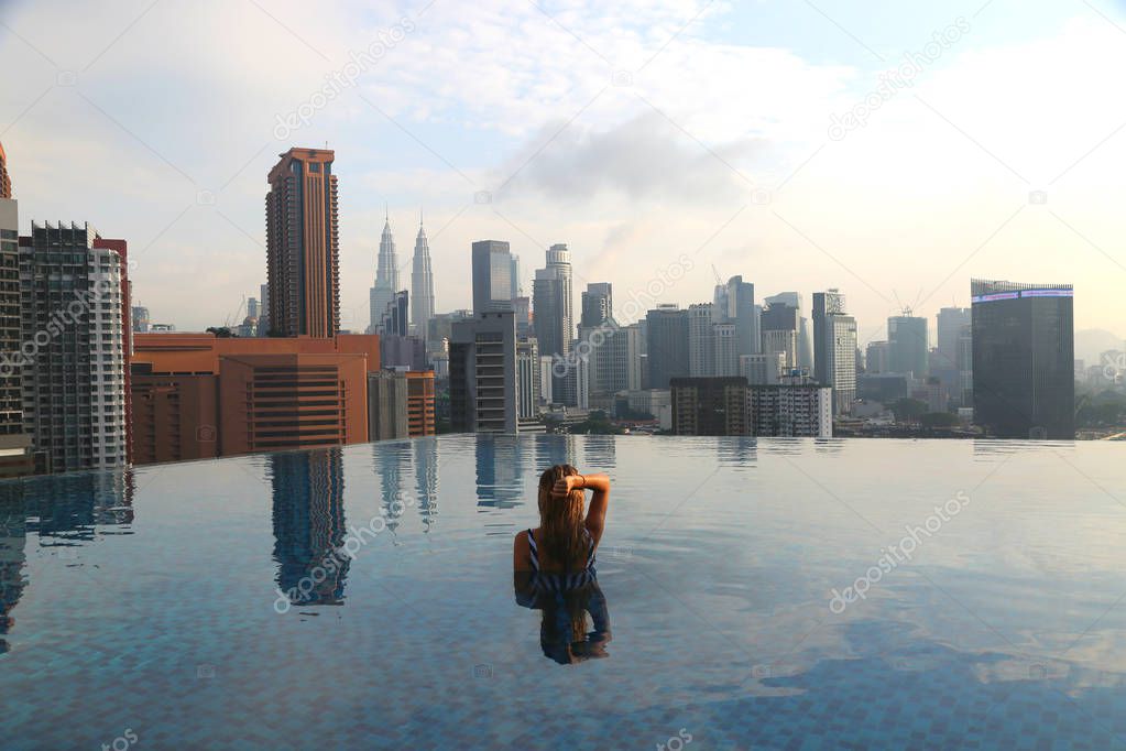 Young happy girl swimming alone in the infinity pool on rooftop early in the morning in Kuala Lumpur in Malaysia.