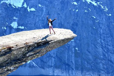 Genç bir kadın Trolltunga 'nın kıyısında dikilirken Norveç' in Odda, Rogaland yakınlarındaki karlı dağlarda kollarını havaya kaldırıyor..