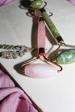 Pembe ve yeşil yüz silindirleri pembe pamuklu arka planda. Yüz masajcıları düz yatıyordu. Güzellik aletleri.