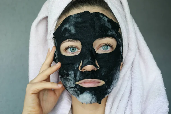 黒炭面マスク 頭に黒い炭酸マスクとタオルを持つ美しい若い女性 顔治療 — ストック写真