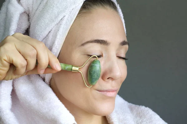 Woman making face massage with green jade roller. Beauty tools  derma roller for face treatment. Funny face.