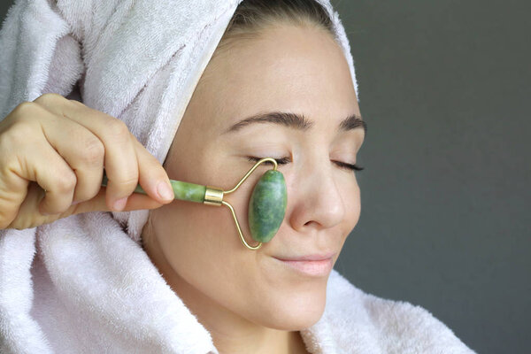 Женщина делает массаж лица зеленой нефритовой розой. Косметические средства дермы для ухода за лицом. Смешное лицо. 