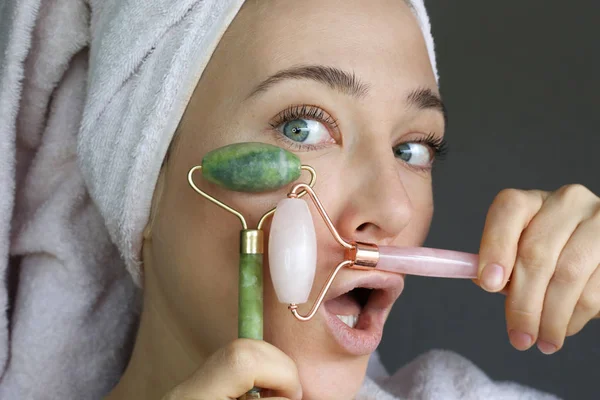 Green jade roller and pink quartz roller face massage. Beauty tools for face treatment. Funny face.