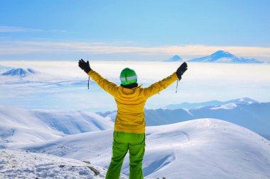 Happy woman in yellow ski jacket standing with hands up on the pick of mountain Tegenis. View of Ararat mountain. clipart