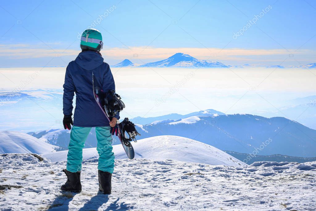 Happy young sportive woman holding snowboard at the top of the mountain Tegenis in Tsaghkadzor ski resort Armenia.