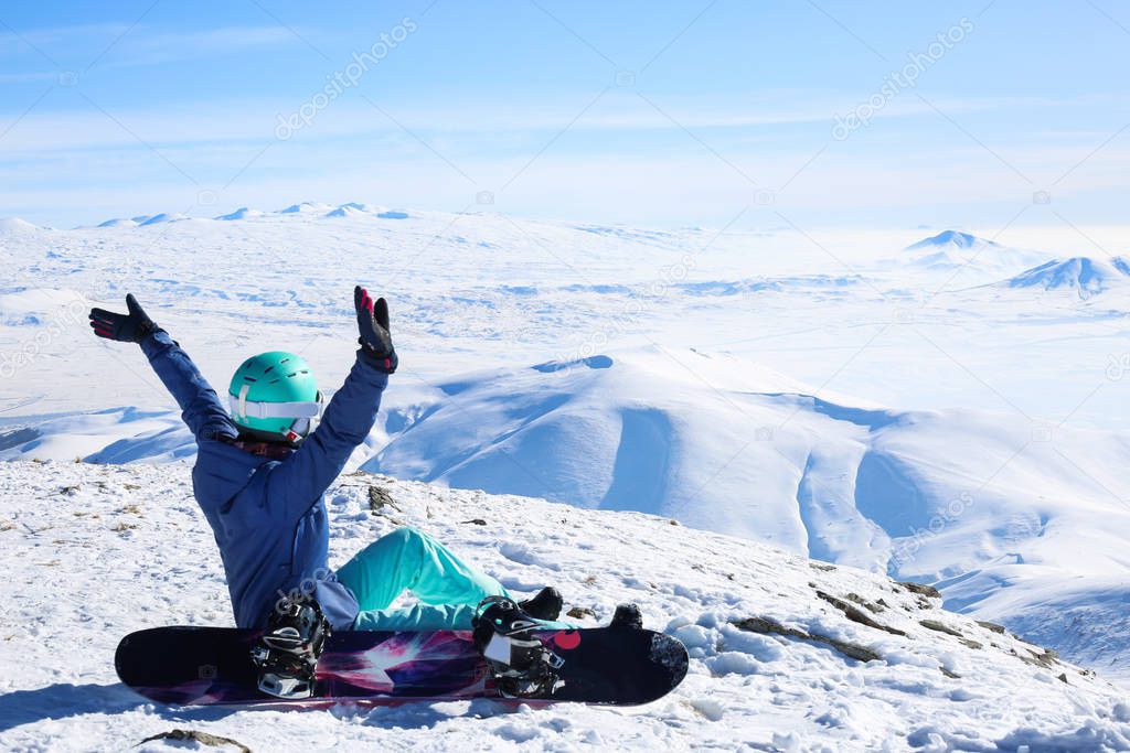 Woman snowboarder hands up sitting at the top of the mountain Tegenis in Tsaghkadzor ski resort Armenia.