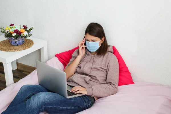 Young woman working at home during quarantine. Sick woman wearing face mask with laptop at home.