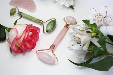 Güzellik masajı terapisi için yeşim yüz silindiri. Çiçek arka planında pembe ve yeşil yüz silindiri. Yüz bakımı. Ev kaplıcası.  