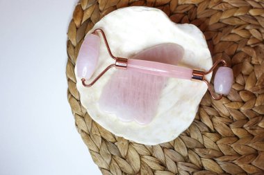 Beyaz arka planda deniz kabuğunda duran pembe kuvars yüz silindiri. Güzellik aletleri. Deri tedavisi cihazı. Deri silindiri.