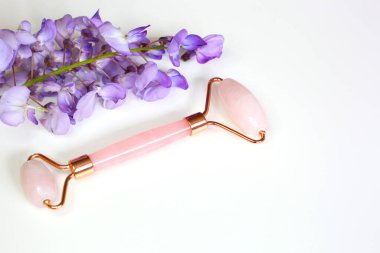 Beyaz arka planda cilt tedavisi için pembe kuvars yüz masajı. Ev spa ayarları.