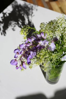 Evdeki güzel bahar çiçekleri. Güneşli bir günde vazo ve çiçekler masanın üzerinde gölgeler. Karşıtlık fikri.