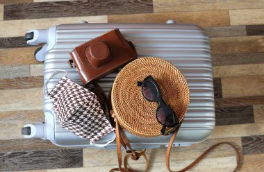 Kadın kıyafetleri ve ahşap zemin üzerinde pamuk maskeli çanta. Corona virüsü salgınından sonra yurt dışına seyahate hazırlanıyoruz. Seyahat konsepti. Önleme yöntemleri.