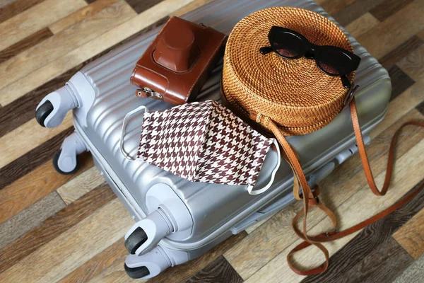 Suitcase hand bag with woman clothes and cotton face mask on wooden floor background. Preparing for trip abroad after corona virus pandemic. Travel concept. Prevention methods.