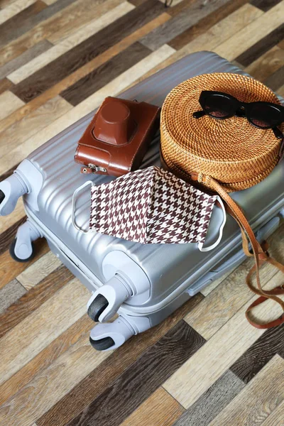 Suitcase hand bag with woman clothes and cotton face mask on wooden floor background. Preparing for trip abroad after corona virus pandemic. Travel concept. Prevention methods.