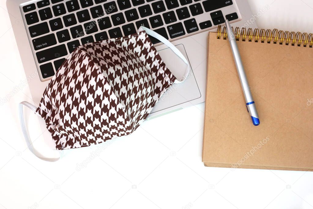 Cotton face mask laying on the laptop. Work from home concept. Stay at home during coronavirus cove 19. Hand made  textile face mask on white background.