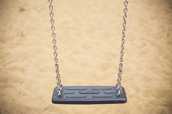 A gray swing with metal chains in the park with the sand in the background