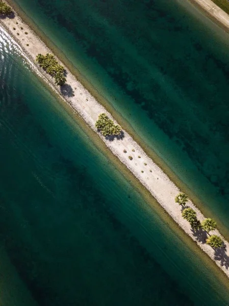 Foto de ángulo alto de una estrecha línea de arena con árboles verdes en medio del mar — Foto de Stock