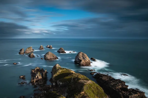 High angle shot of the sea with big rocks in the water under a blue cloudy sky — 스톡 사진