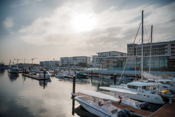 The sailing boats by the wooden pier with the buildings in the background under the cloudy sky