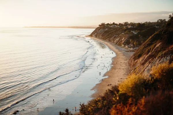 Beautiful shot of people walking in a wild seashore next to low hills — Stock Photo, Image