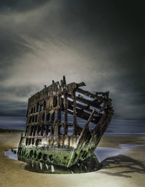 Wreck of the Peter Iredale reflected in a water surface under the breathtaking clouds clipart