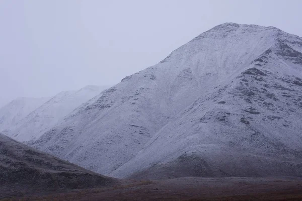 A low angle shot of snowy mountains covered in fog in the Gates of the Arctic National Park