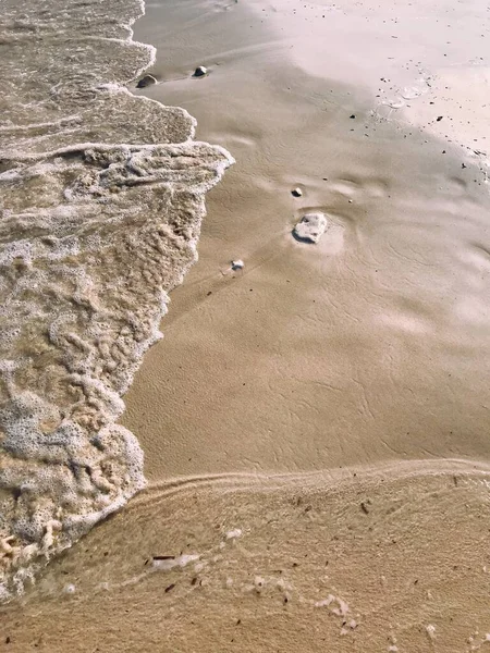 A vertical shot of the waves coming to the beautiful sandy beach