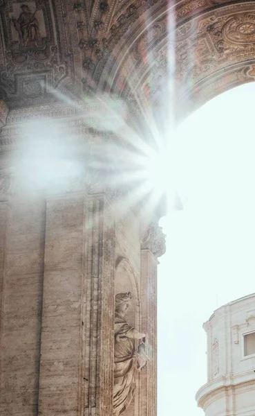 Foto vertical de un hermoso arco con esculturas con el sol brillante en el fondo — Foto de Stock